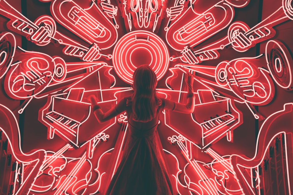 Eine Person steht vor einer Wand mit leuchtenden, gemalten Instrumenten, die rot leuchten.