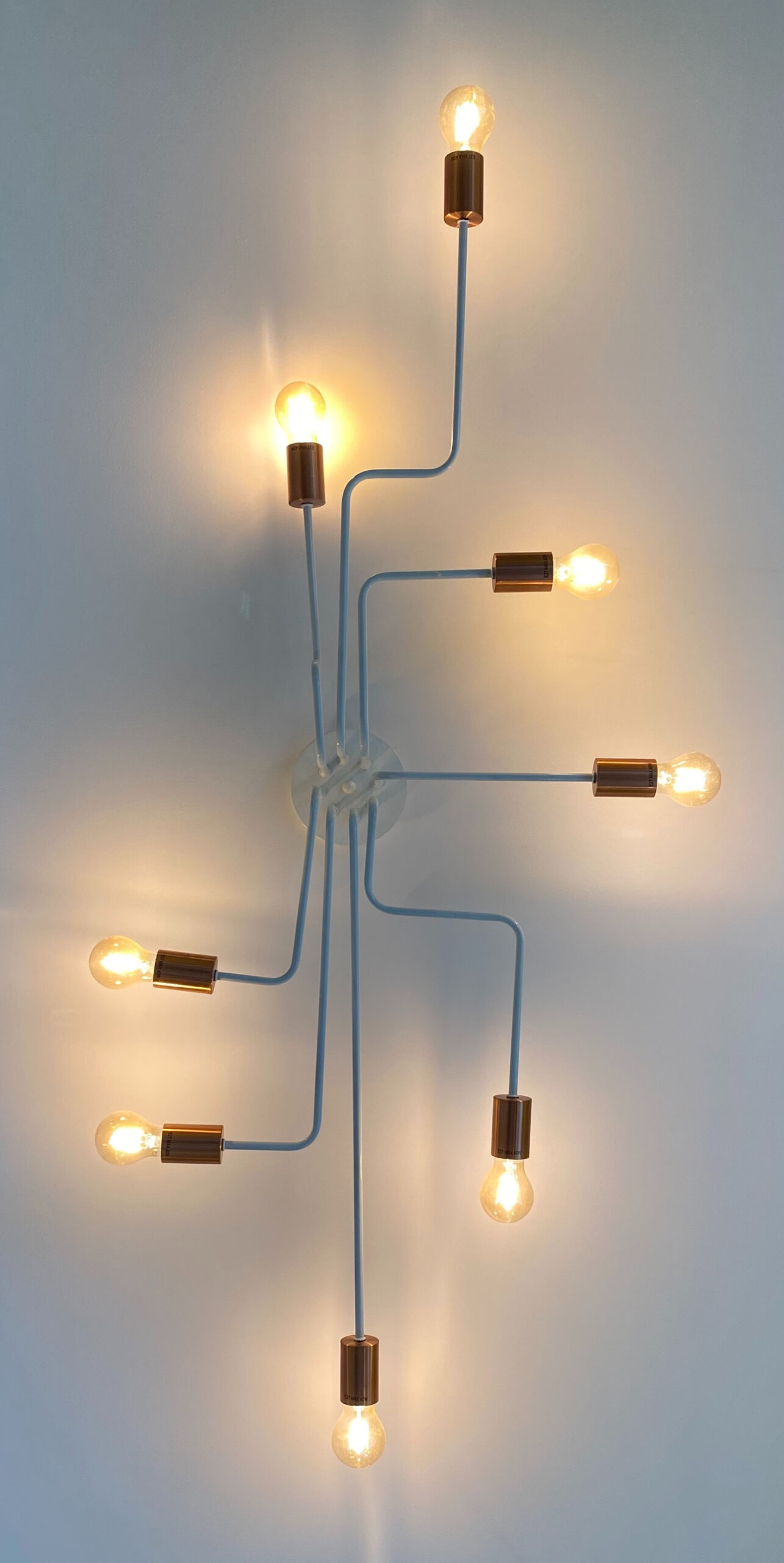An einer Wand hängt eine Lampe, die acht Arme und am Ende jeweils eine Glühbirne hat.